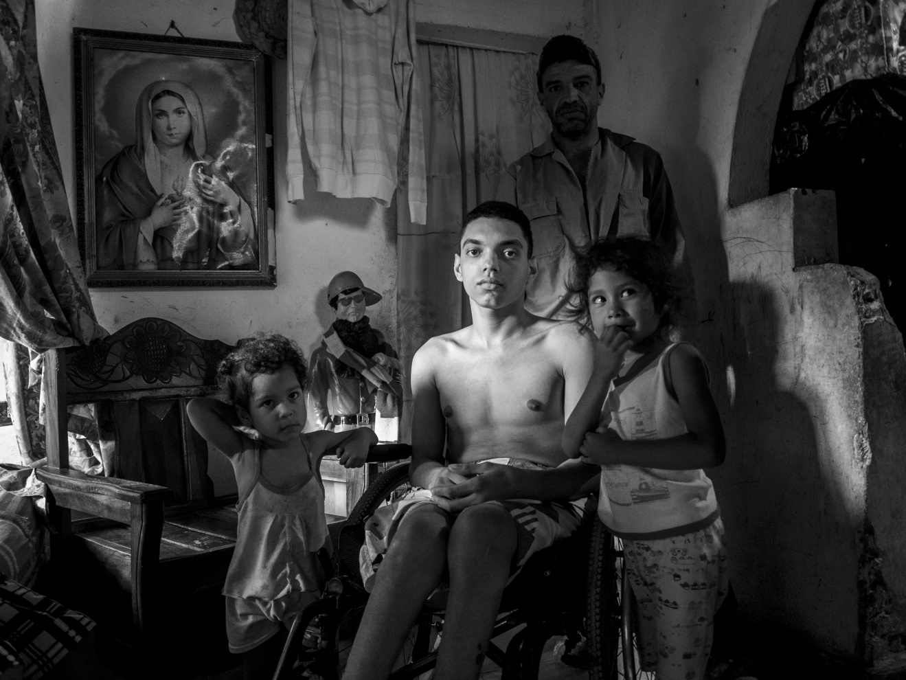 Venezuela; Miranda; Petare; 2015

A family portrayed in their own home. The young boy,  injured by a gun shot sits on a wheelchair. Petare, one of South America’s largest slums, is located just outside Caracas, Venezuela’s capital city. During the night, the city becomes what is considered one of the most dangerous areas of Venezuela, counting the highest number of homicides per year.